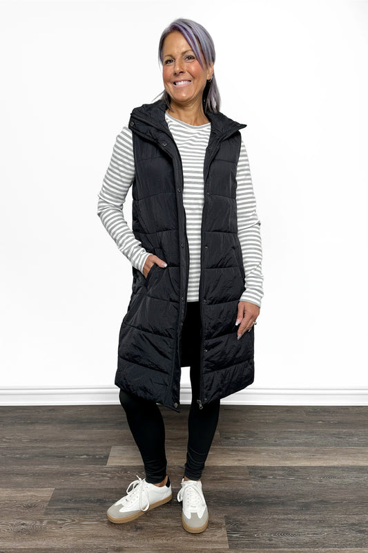Woman wearing a black puffer vest over a striped shirt on a white background