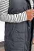 Person wearing a dark gray puffer vest with a striped shirt underneath.