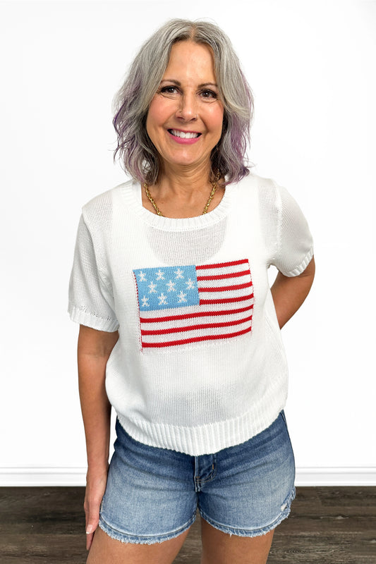 Woman wearing a white sweater with an American flag design and denim shorts on a white background