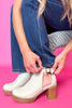 Person wearing white ankle boots with wooden soles on a pink background