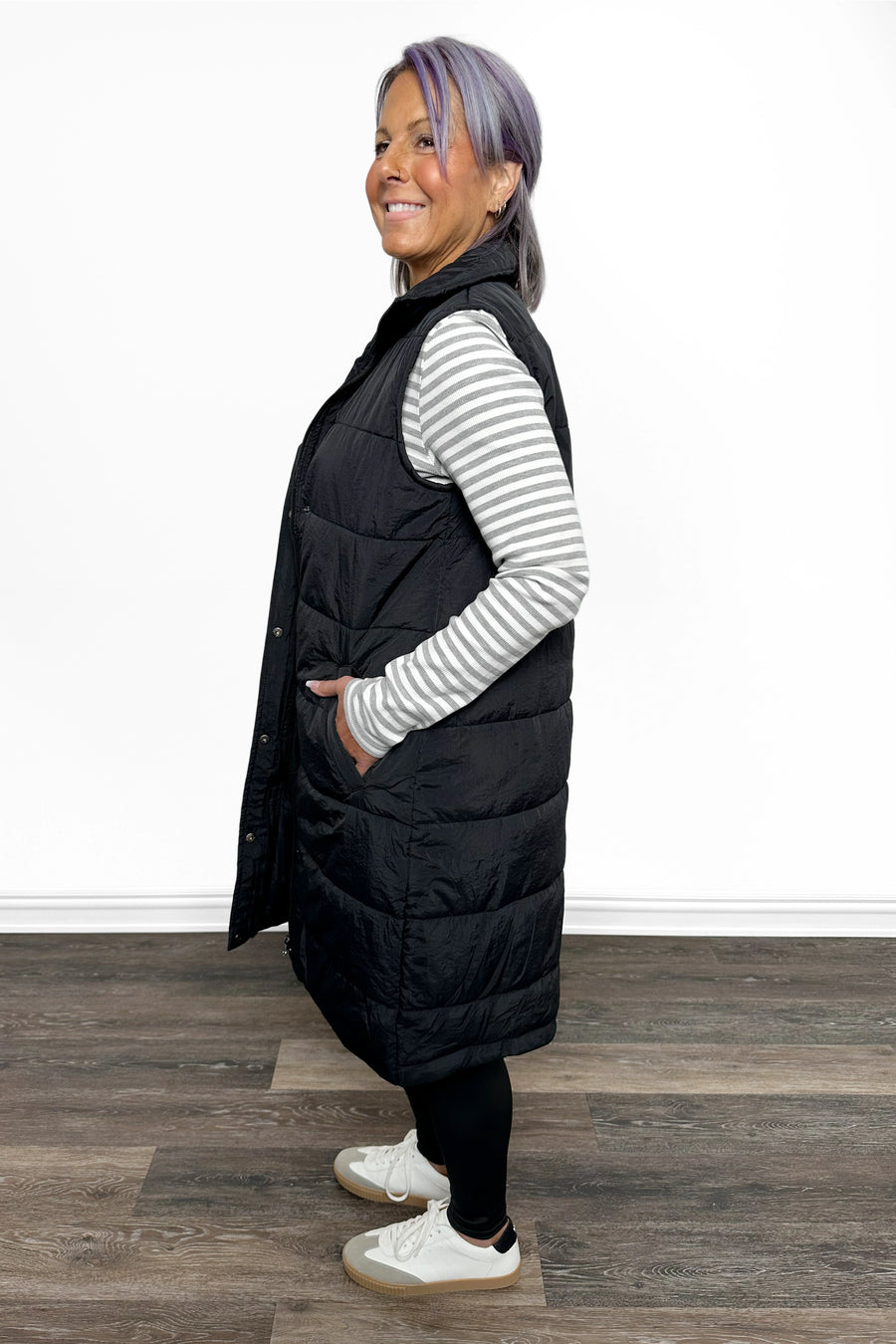 Person wearing a black puffer vest over a striped shirt on a wooden floor.