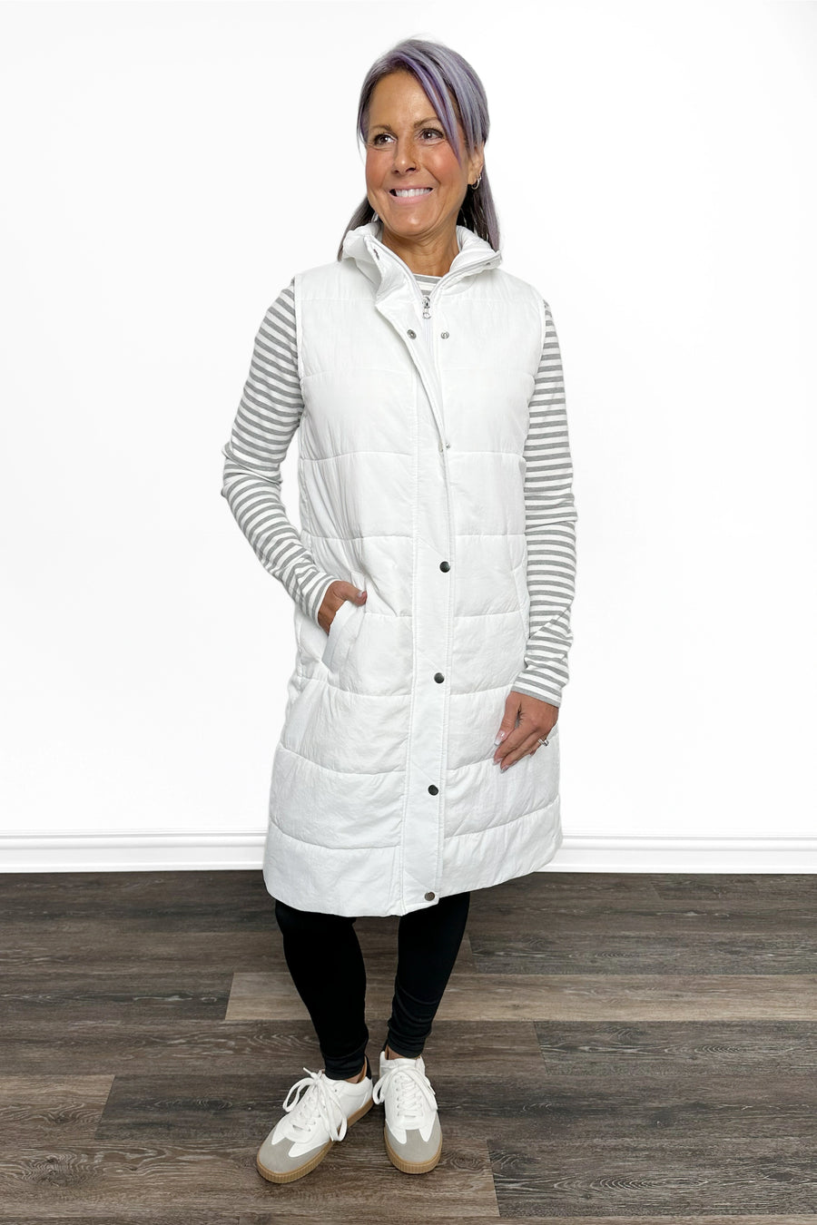 Woman wearing a long white puffer vest over a striped shirt on a wooden floor.