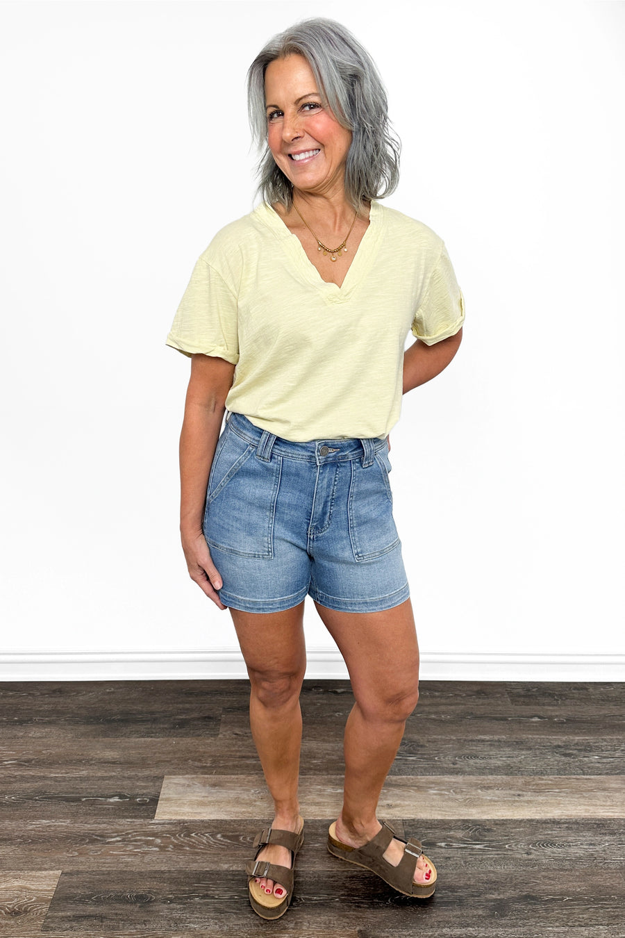 Woman wearing a yellow shirt and blue shorts standing on a wooden floor.