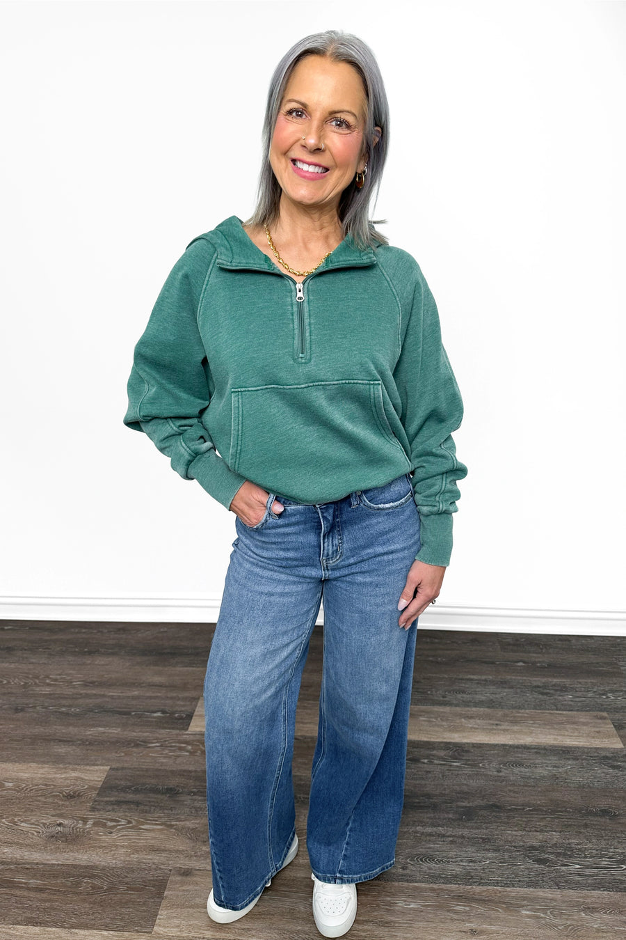 Woman wearing a green fleece pullover and blue jeans standing on a wooden floor.