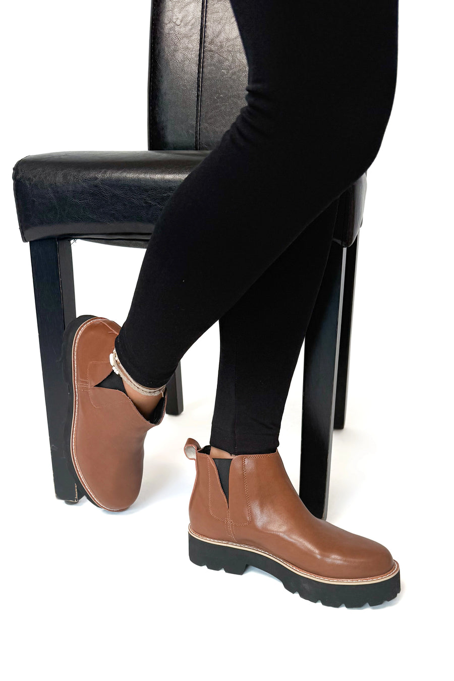 Brown Chelsea boots worn with black pants on a white background
