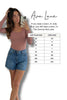 Woman taking a selfie wearing a pink top and blue shorts, with a size chart for Ava Lane clothing on a white background.